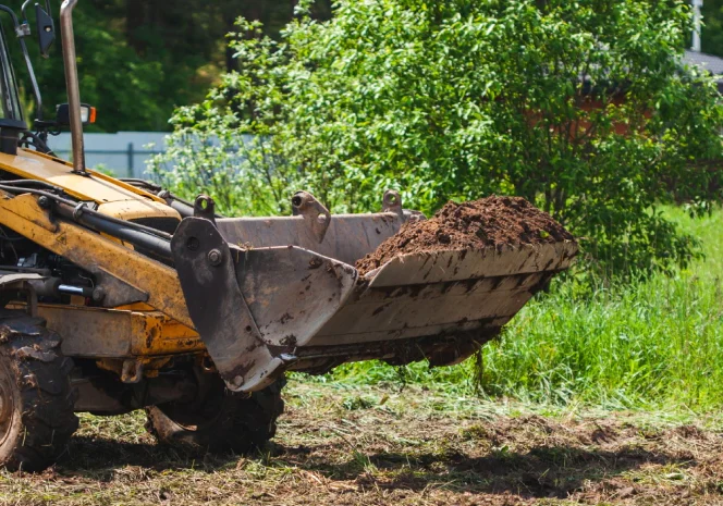 skid steer picking up some dirt of a field with grass around